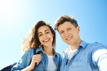 happy smiling couple, attractive man and woman looking in the camera at the sky background. bottom view