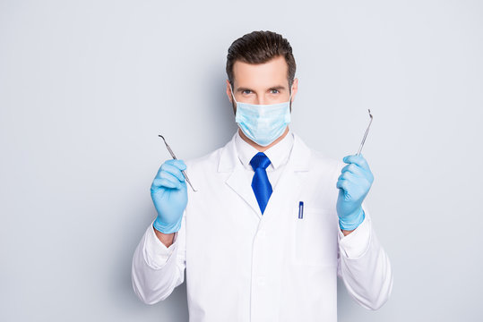 Portrait of successful handsome dentist in white lab coat with blue tie having, showing, holding tools for teeth treatment with hands, looking at camera, isolated on grey background