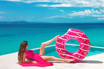 Sexy brunette Girl relaxing with inflatable float ring by the hotel infinity pool at exotic island. Travel vacation carefree woman enjoying sumer vaction. Tropical beach lifestyle.
