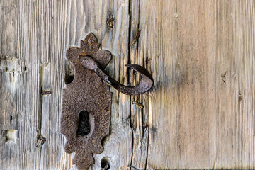 Foreground of old wooden door with iron handle. Old rusty gate handle on wooden door.
