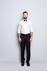 Full size fullbody portrait of serious handsome croupier in white shirt, bowtie, black pants, formalwear, looking at camera, isolated on grey background