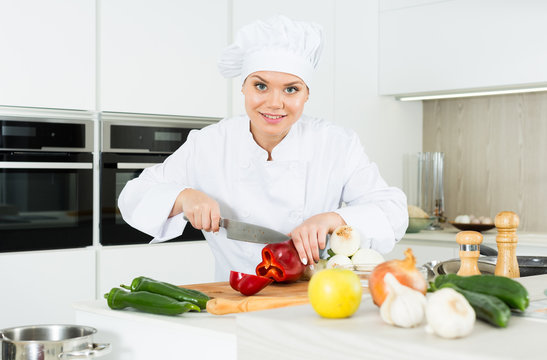 Smiling woman kitchener in uniform is cutting vegetables for salad in the kitchen