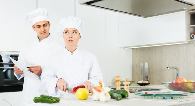 Man and woman kitcheners in uniform are cutting vegetables for salad in the kitchen