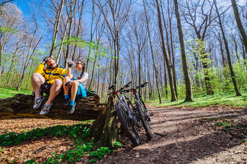 couple sit on stump resting after cycling by forest
