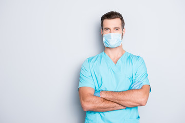 Portrait with copyspace, empty place of attractive handsome man in sterile mask and blue lab uniform, having his arms crossed, looking at camera isolated on grey background