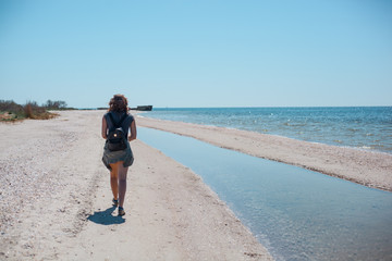 girl on a sea beach with a backpack and glasses in the background of a sunken ship