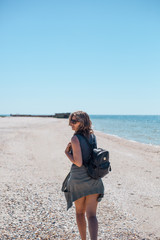 girl on a sea beach with a backpack and glasses in the background of a sunken ship