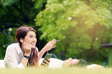 Couple of asian lovers listening a music while relaxing in a public park sitting on grass sward.Business and Music concept.