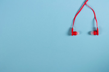 Red new earphone with cable on blue paper background with copy space