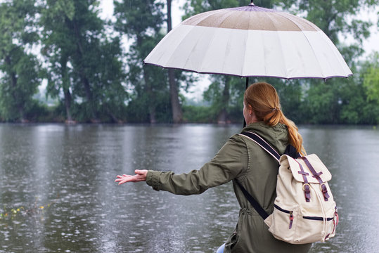 Woman with umbrella and backpack standing in rain on the riverside
