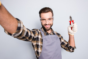 Self portrait of joyful cheerful man with stubble shooting selfie on front camera, showing pliers...