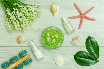 Bottles with cream for face skin and aromatic oil, hand massager, bowl with sea salt, starfish, sea shell and bouquet of lilies of the valley