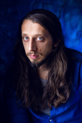 man with long hair and beard sits at home on a chair by the window