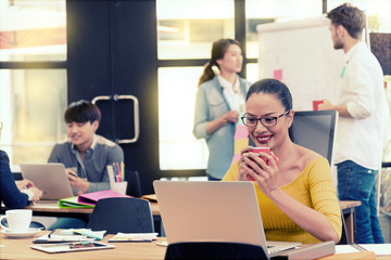 Fototapeta premium Asian charming beautiful business woman holding a cup of coffee between working in modern office and blurred multi ethnic business person group in casual suit in background. 