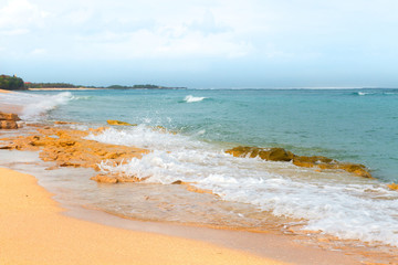 South Asian tropical beach with yellow sand, azure ocean with foamy waves, green trees and colorful blue sky