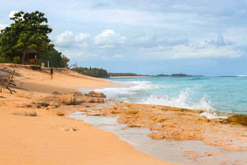 South Asian tropical beach with yellow sand, azure ocean with foamy waves, green trees and colorful blue sky