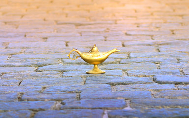 Bronze Aladdin lamp on cobbles. Fairy tale oriental concept of fulfillment of desires.