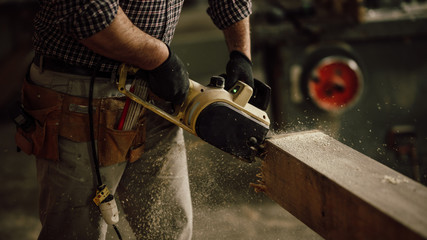 carpenter in the workshop saw a piece of wood with an electric chainsaw