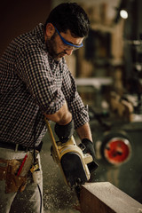 carpenter in the workshop saw a piece of wood with an electric chainsaw