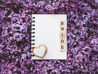 Heart-shaped cookie, covered with bright glaze, word BRIDE, sketchbook with a blank page for Your inscription on the background flowers. Top view, close-up. Congratulations for relatives, loved ones