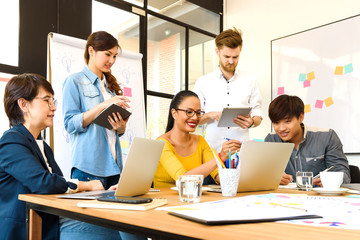 Asian young man business officer explaining internal meeting to his project team in modern office. They are the multi ethnic business person group in casual suit. Project and Business concept.