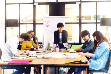 Asian young man business officer explaining internal meeting to his project team in modern office. They are the multi ethnic business person group in casual suit. Project and Business concept.
