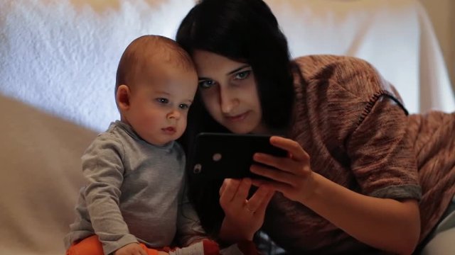Young beautiful woman is showing the child a smartphone. The little boy looks closely at the image on the screen of the smartphone.