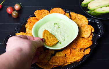 Hand dipping tortilla chips into green dip