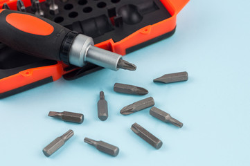 One screwdriver with handle of black and orange color near scattered metal bits and plastic box for bits on blue background