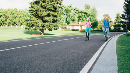 elderly couple riding bicycles, on a wide road in the city park, Europe