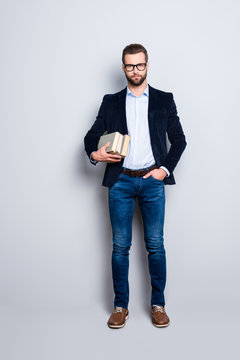 Full size fullbody portrait of attractive stylish teacher in shirt, jacket, jeans with stubble having three books, holding hand in pocket, looking at camera isolated on grey background