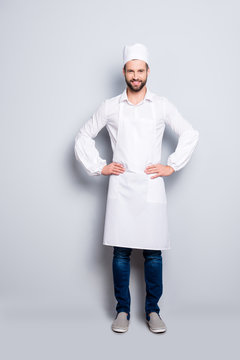 Full Size Body Portrait Of Attractive Handsome Butcher Isolated Over Grey Background, Wearing White Shirt, Apron, Jeans, Sneakers, Holding Arms On Waist