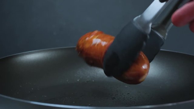 Sausages are fried in a frying pan. Sausage inverted with forceps. Grill. 4k
