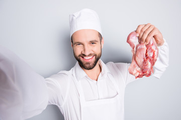 Self portrait of successful joyful butcher with stubble shooting selfie on front camera and holding...