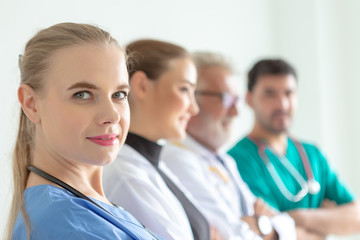 Confident female doctor looking at camera and smiling while her colleagues standing in a row behind her. A team of experienced highly qualified doctors.