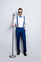 Full size full body portrait of cheerful elegant singer with bristle in blue outfit white shirt holding hand in pocket, having mic, isolated over grey background
