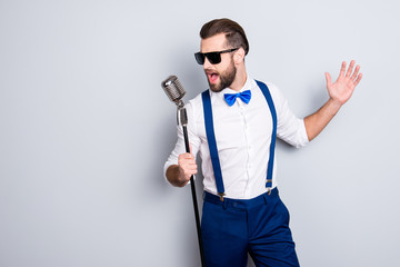 Portrait of handsome attractive singer in blue pants with suspenders and black glasses, singing hit...