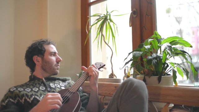 A Man play on a Mandoline near the Window at Home in Living Room - Day