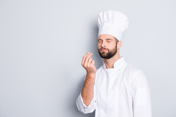 Portrait with copyspace, empty place for advertisement, product of attractive chef cook in beret with close eyes, white outfit making bellisimo symbol, sign with fingers, isolated on grey background