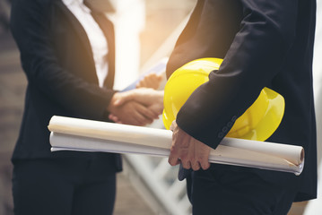 Business people Handshake (shaking hands)with partnership at construction site,Engineer holdind drawings and safety hat greeting,successful after signing contract and dealing.