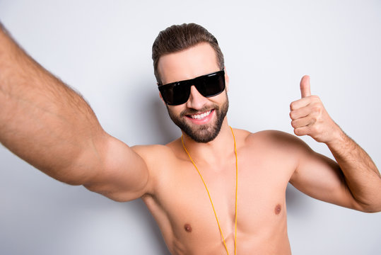 Self portrait of cheerful joyful lifeguard with stubble shooting selfie on front camera showing thumb up sign isolated on grey background