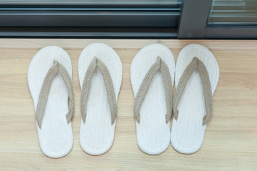 Two pairs of white sandal slippers arrange on laminate floor for couple lover to use in house.