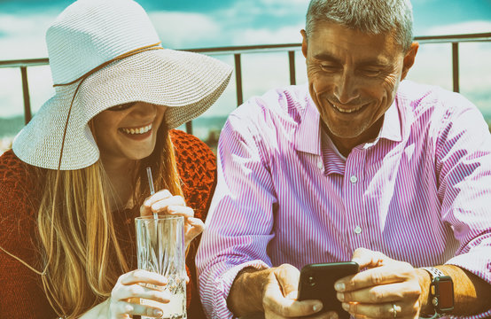 Happy couple on a city rooftop smiling reviewing holiday pictures, vintage filtered