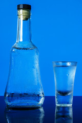 Bottle with glass of vodka on blue background