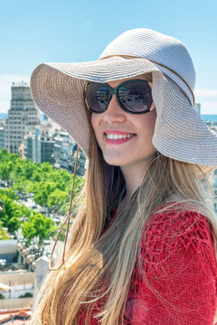 Happy beautiful blonde girl with straw hat looking at city skyline from a rooftop. Holiday concept
