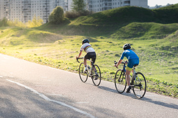 Active male athlete riding bicycles on an open asphalt road. Hills with green grass and the sunset