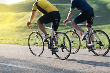Active male athlete riding bicycles on an open asphalt road. Hills with green grass and the sunset - 205263295