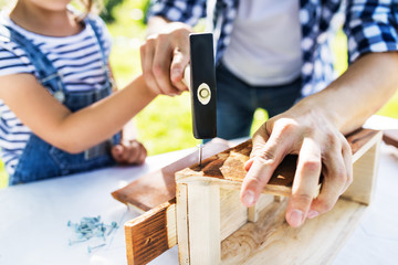 Father with a small daughter outside, making wooden birdhouse.