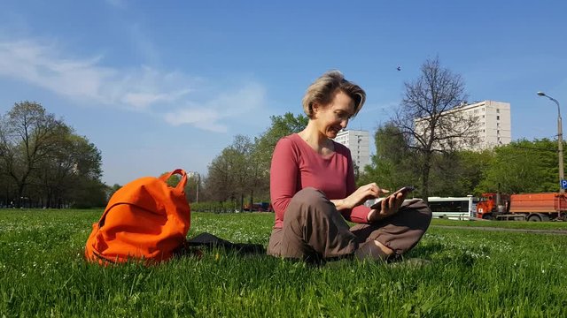 Adult Woman sitting on green grass with mobile phone