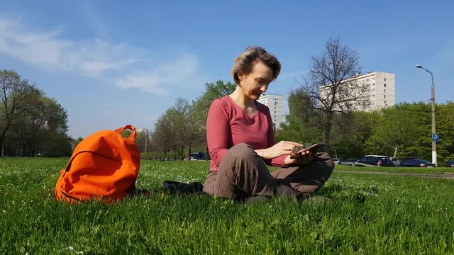 Adult Woman sitting on green grass with mobile phone